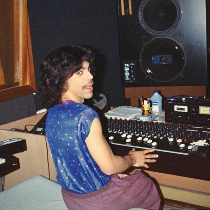 Prince seated at a mixing console in a studio, looking back over his shoulder